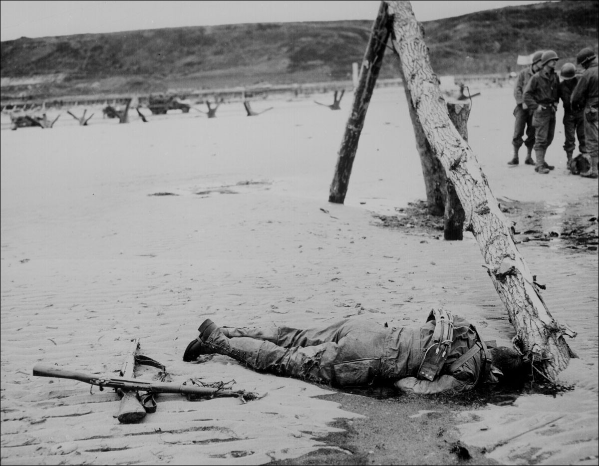 Crossed rifles in the sand are a comrade's tribute to this American soldier on a beach in Normandy.